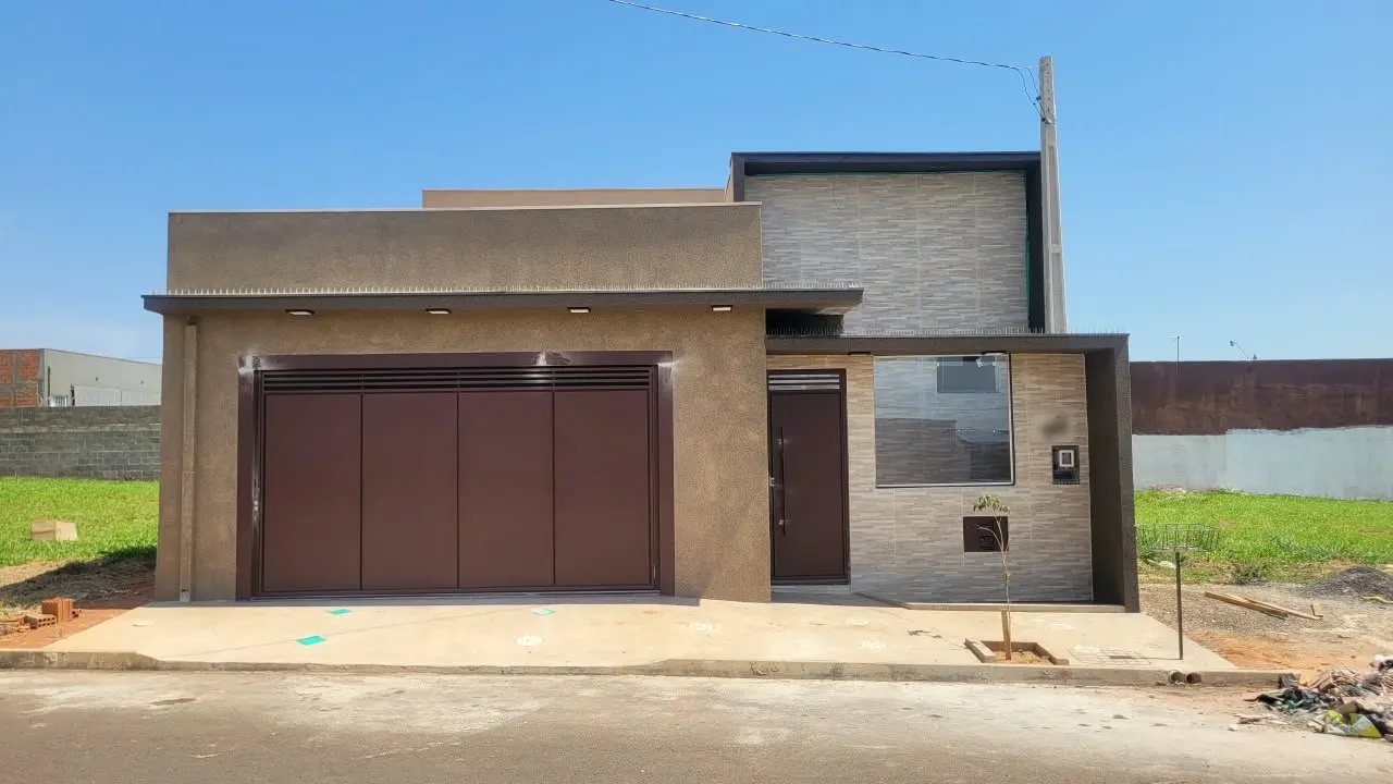 Fachada de casa térrea moderna recém entregue, com portão de garagem marrom, revestimento cinza que imita pedra e luzes embutidas na platibanda.